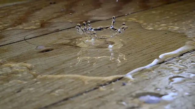 Water pooling on wood floor planks with a droplet splash and swollen board seams