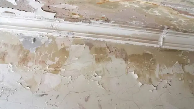 Wall with cracked, peeling paint and brown water staining above the trim