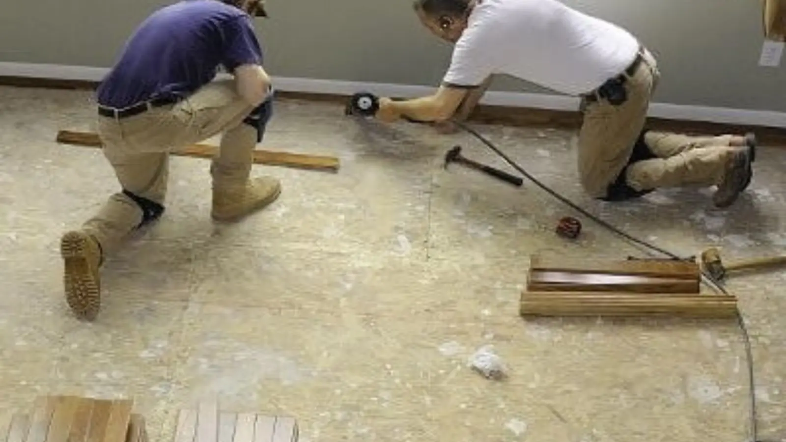 Two workers kneeling on a stripped subfloor installing replacement flooring during a water damage repair
